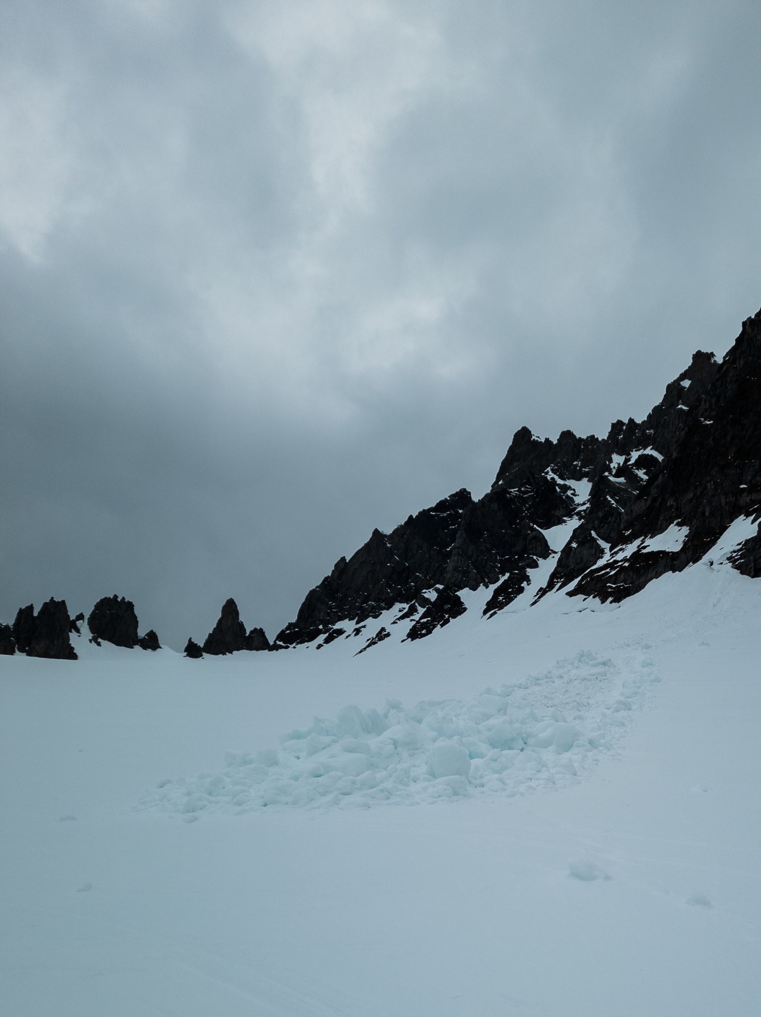 Ujevn snø og oppsamlede snømasser under en mørk og taggete fjellrygg