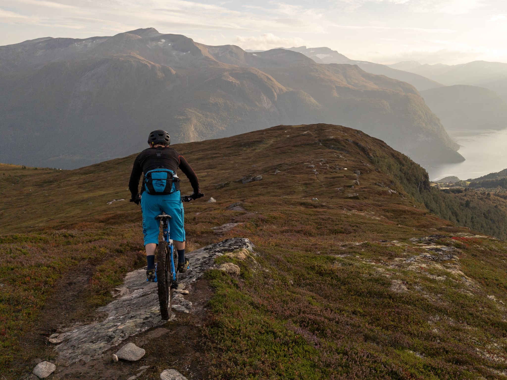 Terrengsyklist følger fjellryggen ned fra Mefjellet med fjord og fjell i kveldssol