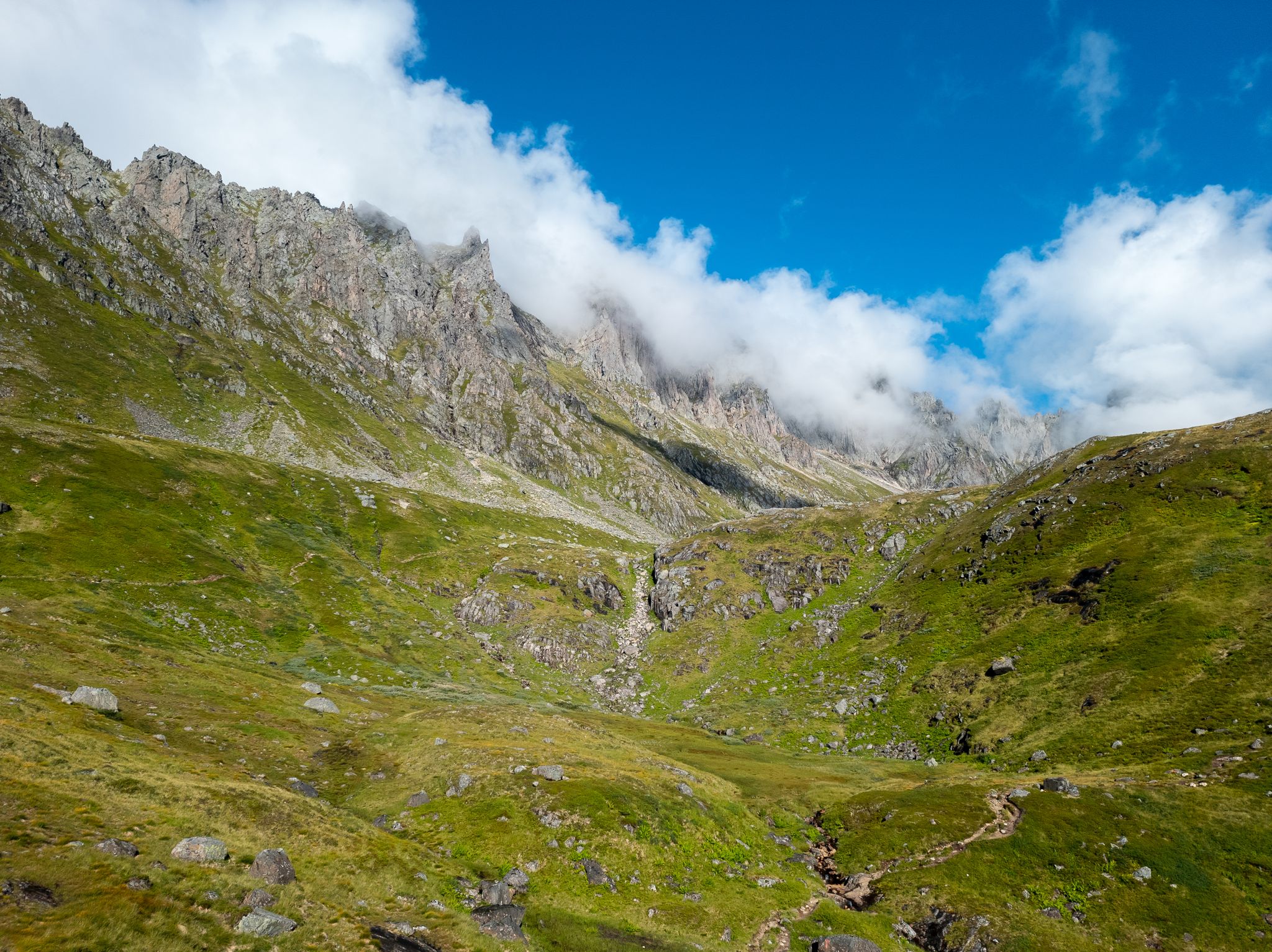 Grønt og steinete terreng i Molladalen under taggete fjell og lave skyer