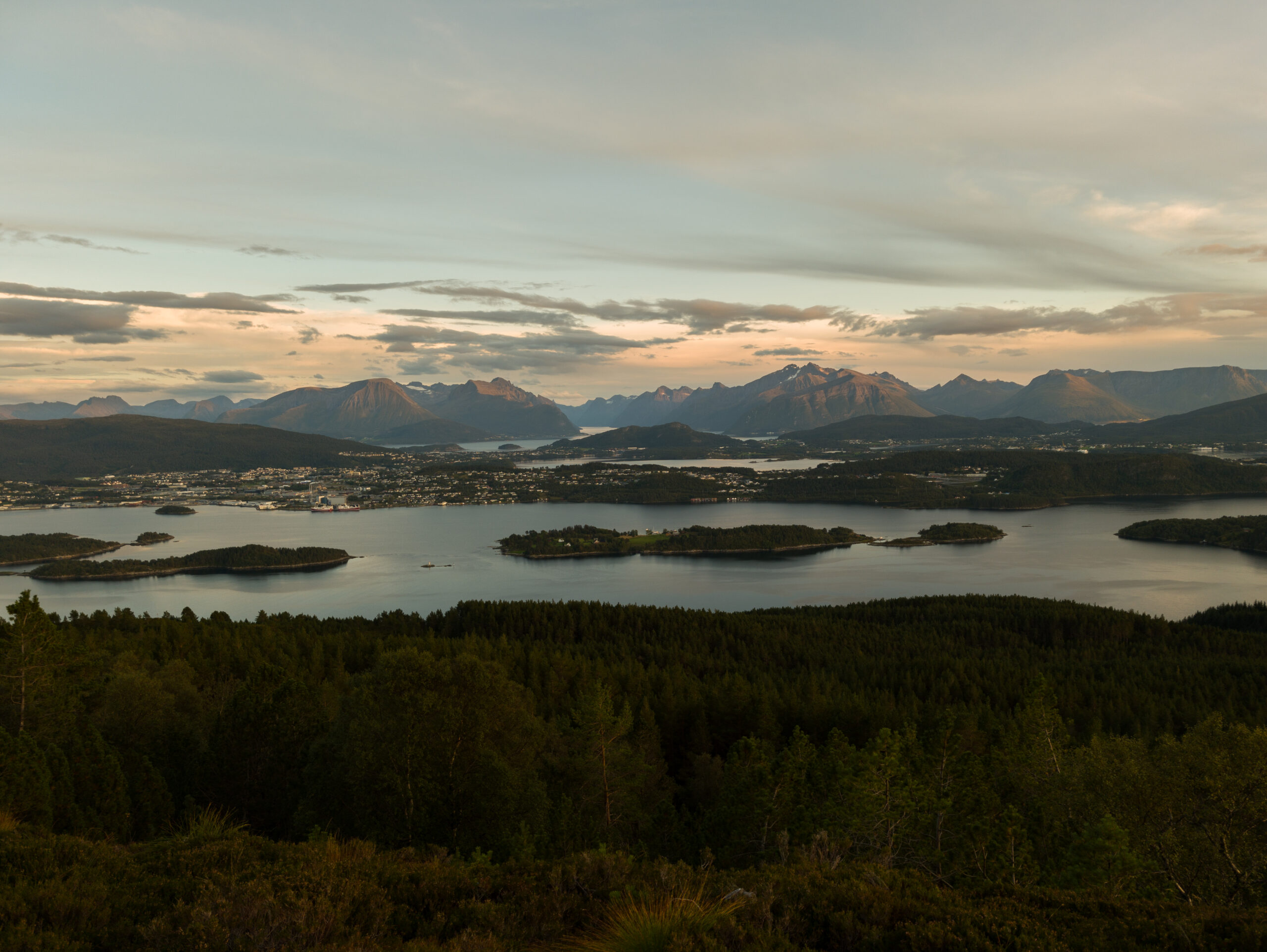 Utsikt fra Myklebusthornet over fjorden, øyene og Sunnmørsfjellene i mykt kveldslys.