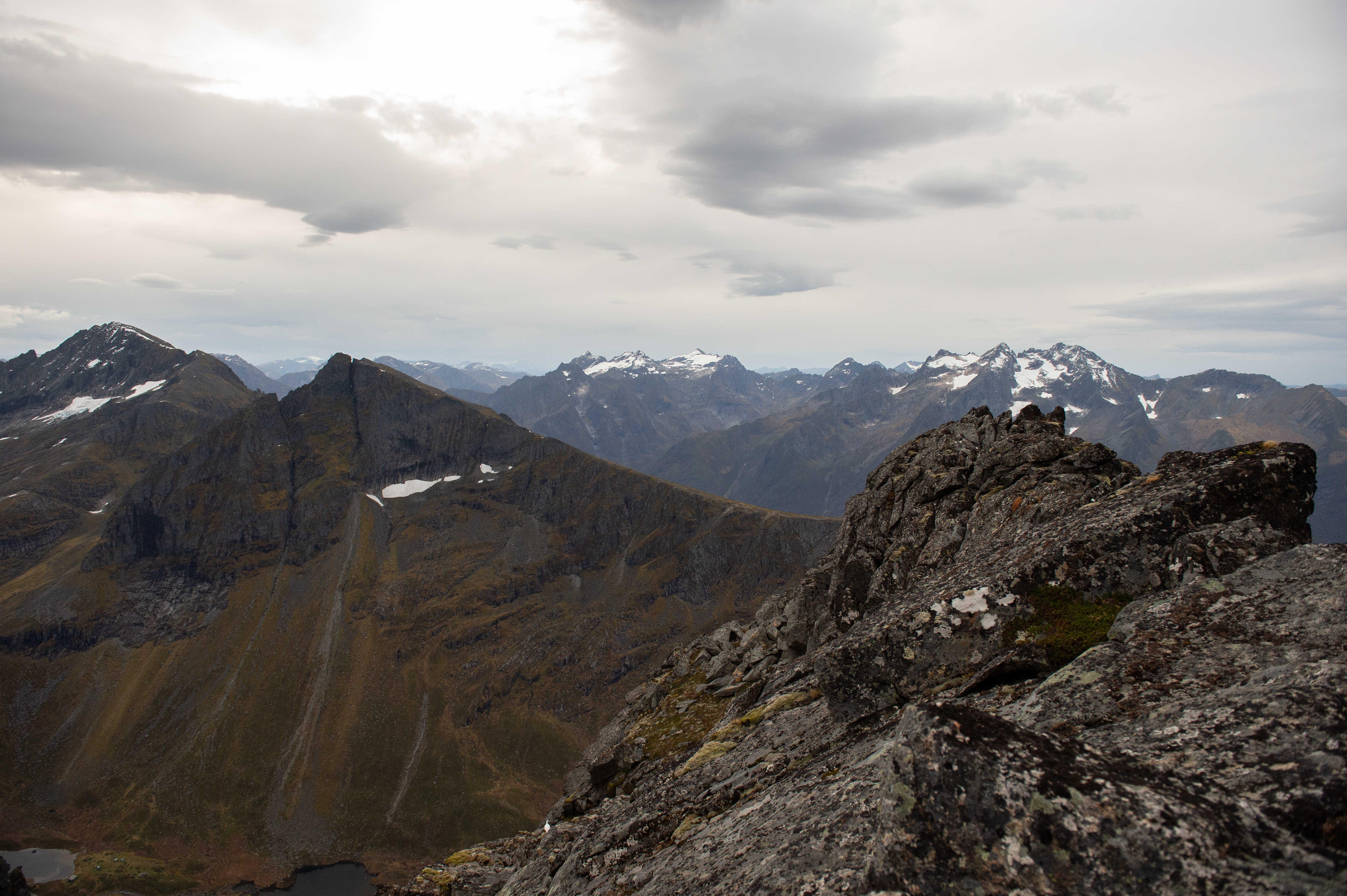 Grove steiner i forgrunnen og fjellrekker med snøflekker sett fra Skopphornet
