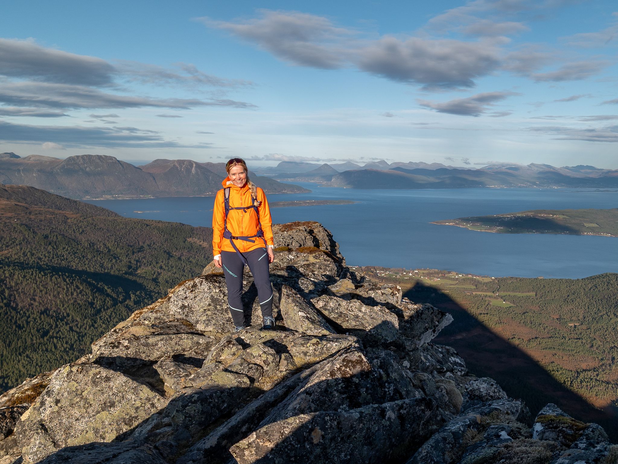 En turdeltaker i oransje jakke på den steinete eggen, med fjorden i bakgrunnen.