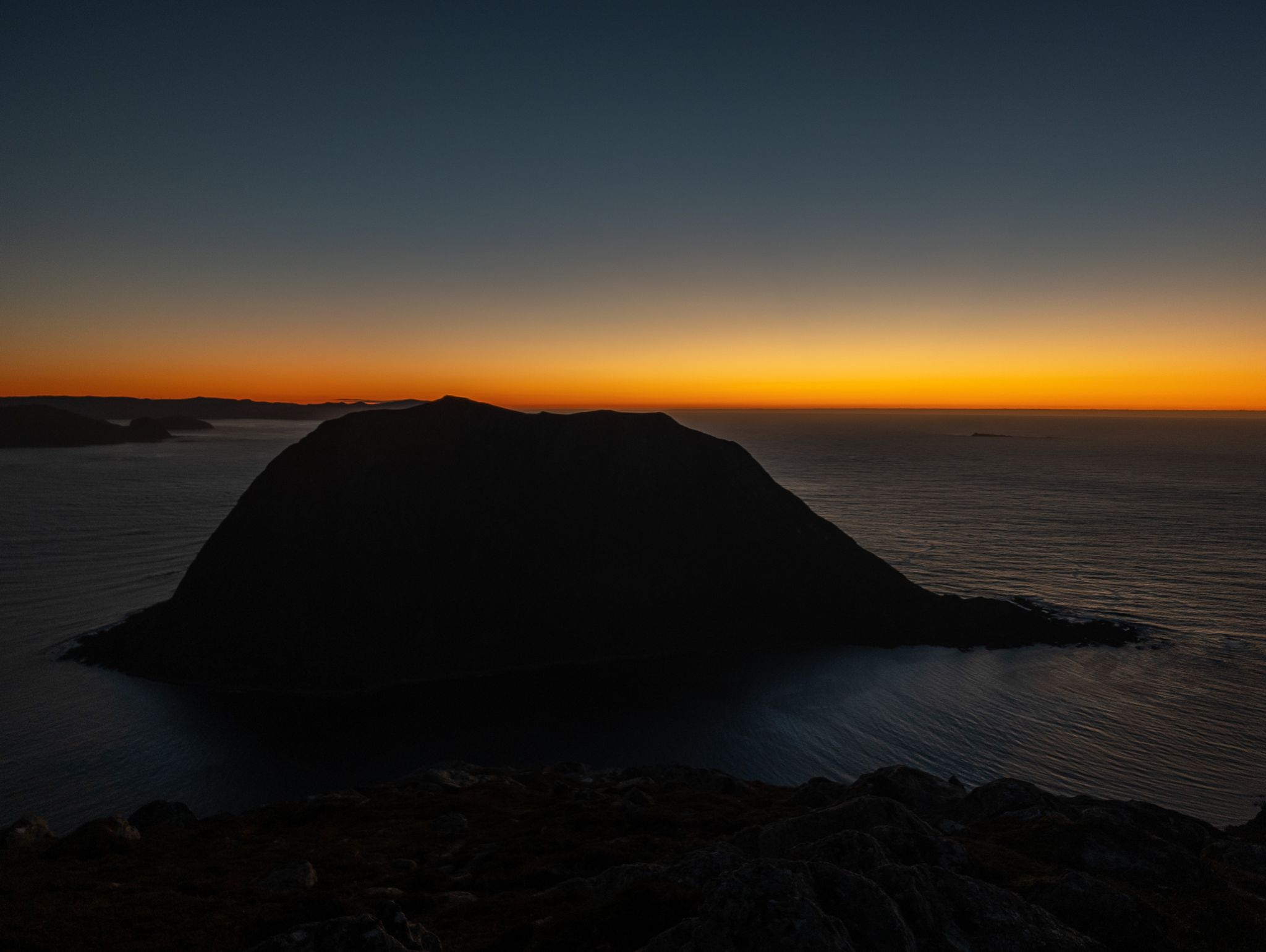 En mørk øyprofil mot havet og et oransje bånd langs horisonten etter solnedgang.