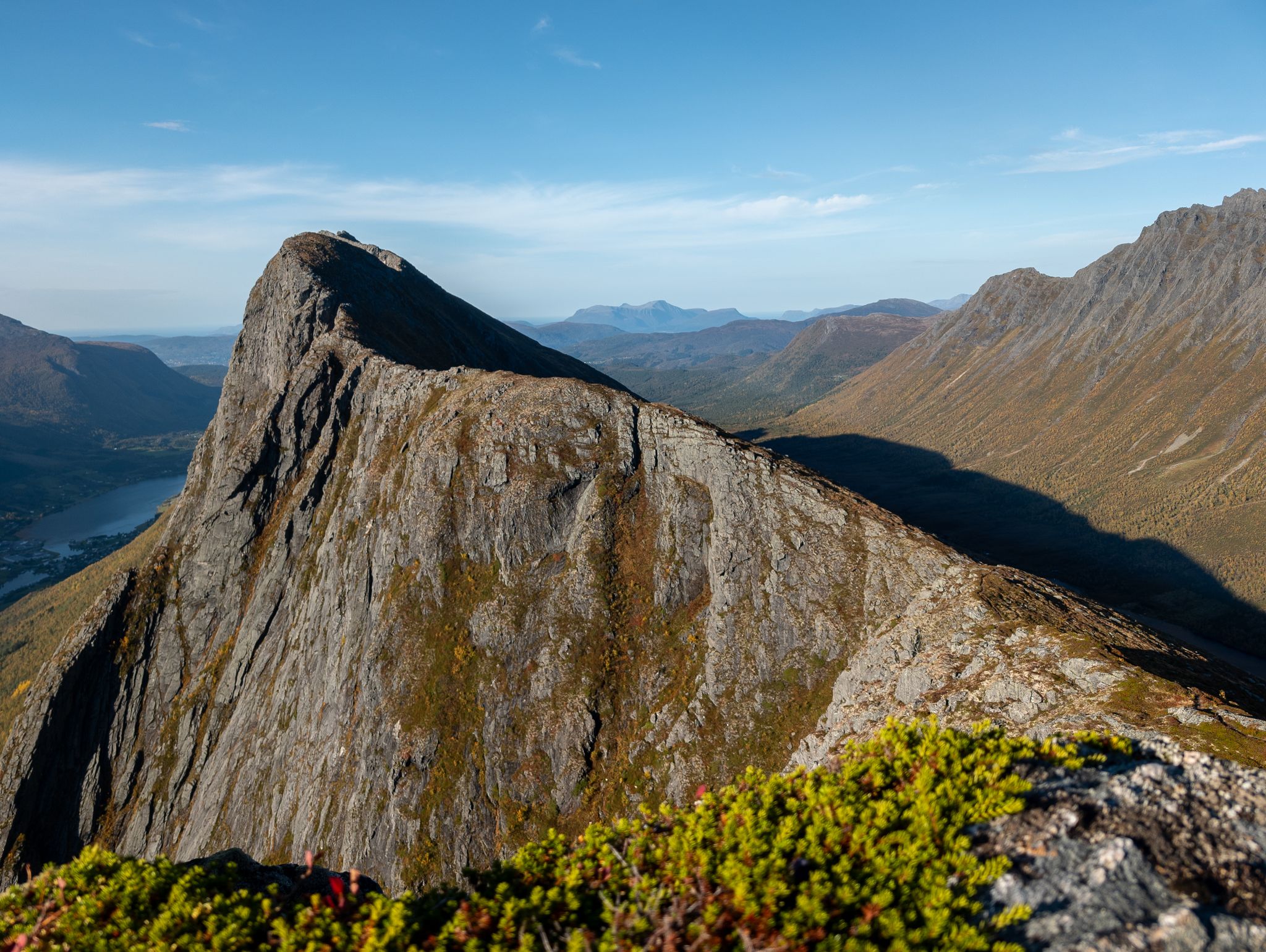 Smal fjellrygg med bratte bergvegger, høstskog og vann i dalen under